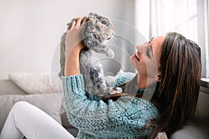 Adorable furry pet bunny rabbit and beautiful woman alone indoors at home, bonding, hugging, smiling, laughing, animal friendship