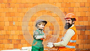 Adorable future architect over a brick background. Little cute son helping his father with building work. Happy team