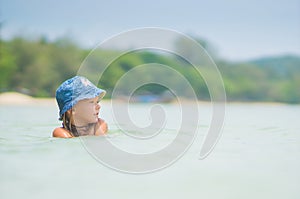 Adorable girl in blue hat swim in ocean near beach