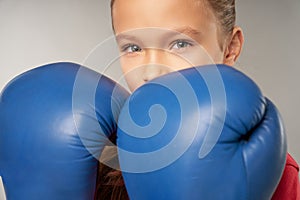 Adorable girl in boxing gloves standing against gray background