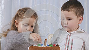 Adorable girl and boy decorates a gingerbread house with a colorful candies