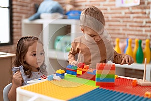 Adorable girl and boy playing with construction block pieces sitting on table at kindergarten