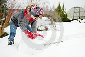 Adorable girl building a snowman in the backyard. Cute child playing in a snow. Winter activities for family with kids