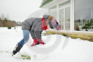 Adorable girl building a snowman in the backyard. Cute child playing in a snow. Winter activities for family with kids