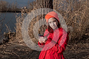 Adorable Girl, dressed in red jacket, poses for making selfie or photo of herself with smartphone