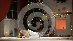 Adorable girl fallen asleep under X-mas tree, waiting Santa, dreaming of gifts