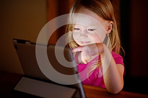 Adorable girl playing with a digital tablet in a dark room
