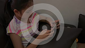 Adorable girl playing games on mobile smartphone and sitting on sofa in living room .