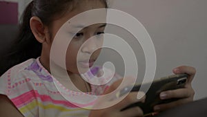 Adorable girl playing games on mobile smartphone and sitting on sofa during quarantine at home.