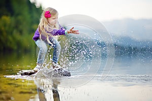 Adorable girl playing by Hallstatter See lake in Austria on warm summer day. Cute child having fun splashing water and throwing st photo