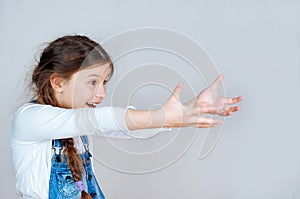 Adorable girl pointing at empty space, emotional portrait. Smiling kid in denim overalls presenting sale discount