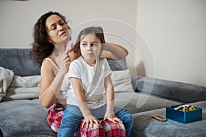Adorable girl sitting on her mother`s legs while she is combing her hair