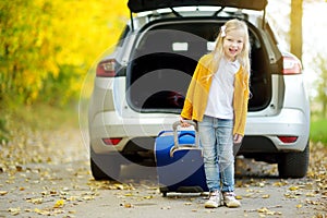 Adorable girl with a suitcase ready to go on vacations with her parents. Child looking forward for a road trip or travel. Autumn b