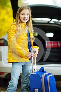 Adorable girl with a suitcase ready to go on vacations with her parents. Child looking forward for a road trip or travel. Autumn b