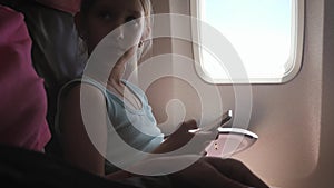 Adorable girl traveling by an airplane and using a digital tablet during the flight. Concept traveling abroad with kids.