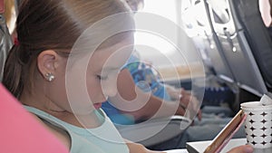Adorable girl traveling by an airplane and using a digital tablet during the flight. Concept traveling abroad with kids.