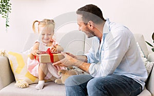 Adorable girl unwrapping gift box from loving father