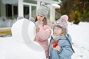 Adorable girls building a snowman in the backyard. Cute children playing in a snow. Winter activities for kids