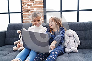 Adorable girls using laptop sitting on sofa at home