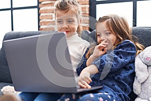 Adorable girls using laptop sitting on sofa at home