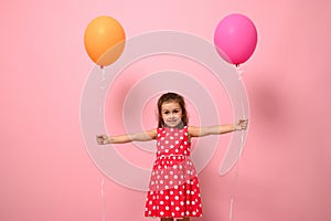 Adorable gorgeous 4 years baby girl in pink dress with white polka dots, holding colorful balloons in her outstretched hands,
