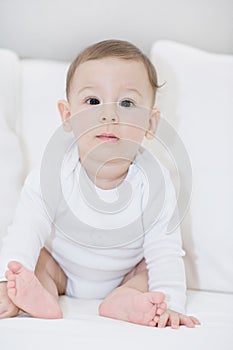 An adorable, happy baby looking at camera on white pillows