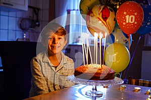 Adorable happy blond little kid boy celebrating his birthday. Child blowing candles on homemade baked cake, indoor