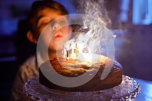 Adorable happy blond little kid boy celebrating his birthday. Child blowing candles on homemade baked cake, indoor