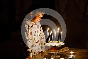 Adorable happy blond little kid boy celebrating his birthday. Child blowing candles on homemade baked cake, indoor