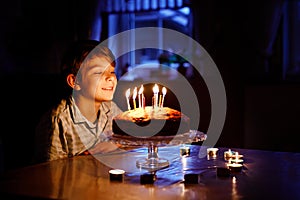 Adorable happy blond little kid boy celebrating his birthday. Child blowing candles on homemade baked cake, indoor