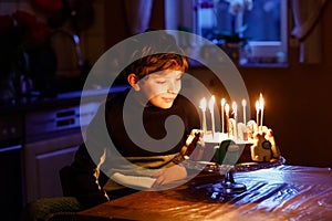 Adorable happy blond little kid boy celebrating his birthday. Child blowing candles on homemade baked cake, indoor