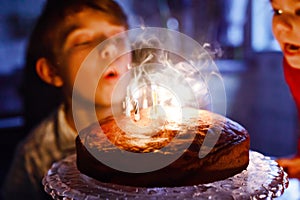 Adorable happy blond little kid boy celebrating his birthday. Child blowing candles on homemade baked cake, indoor