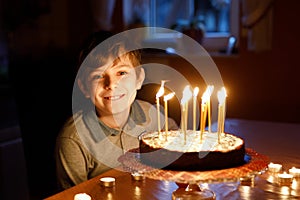 Adorable happy blond little kid boy celebrating his birthday. Child blowing candles on homemade baked cake, indoor