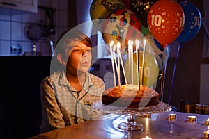 Adorable happy blond little kid boy celebrating his birthday. Child blowing candles on homemade baked cake, indoor