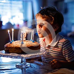 Adorable happy blond little kid boy celebrating his birthday. Child blowing candles on homemade baked cake, indoor