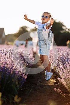 Adorable happy child girl is having fun and jumping in lavender field on summer warm day. Hyperactive smiling little kid