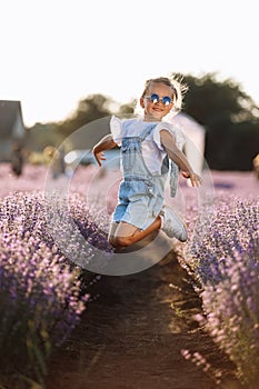 Adorable happy child girl is having fun and jumping in lavender field on summer warm day. Hyperactive smiling little kid