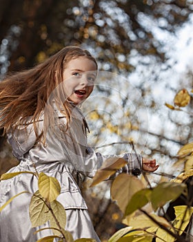 Adorable happy child girl throwing the fallen leaves up, playing in the autumn park
