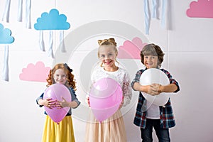 adorable happy kids holding balloons and smiling at camera at birthday