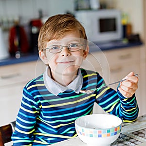 Adorable Happy little blond kid boy with glasses eating homemade cereals for breakfast or lunch. Healthy eating for
