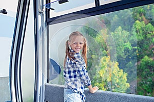 Adorable happy little girl in the cabin on the cable car in mountains in the background of beautful landscape