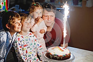 Adorable happy little kid boy celebrating his birthday. Child blowing candles on cake. Father, brother and baby sister