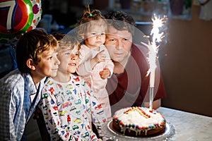 Adorable happy little kid boy celebrating his birthday. Child blowing candles on cake. Father, brother and baby sister