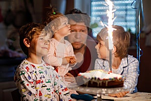 Adorable happy little kid boy celebrating his birthday. Child blowing candles on cake. Father, brother and baby sister