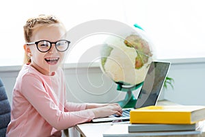 adorable happy schoolchild in eyeglasses studying with laptop and books