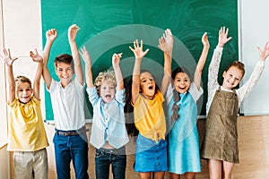 adorable happy schoolchildren with raised hands standing in front of