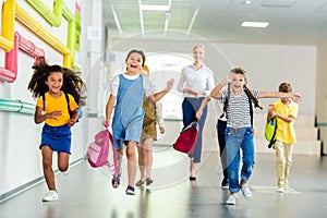 adorable happy schoolchildren running by school corridor together with teacher