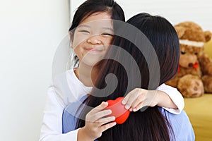 Adorable happy smiling daughter girl hugging her mother with love, cute Asia child holding red heart with mom back, warm love in