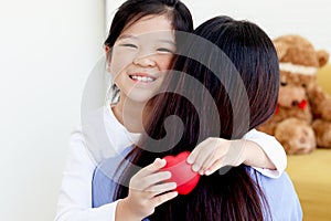 Adorable happy smiling daughter girl hugging her mother with love, cute Asia child holding red heart with mom back, warm love in