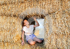 Adorable happy smiling ittle girl child sitting on a hay rolls in a wheat field
